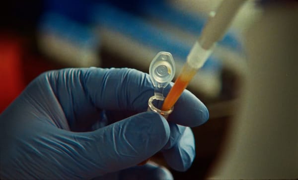 A gloved hand pipetting into a sample tube in a laboratory, from Anthropic's enzyme discovery announcement