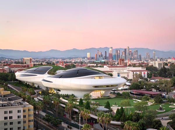 The white, curving Lucas Museum of Narrative Art building in Exposition Park at dusk, with the downtown Los Angeles skyline behind it